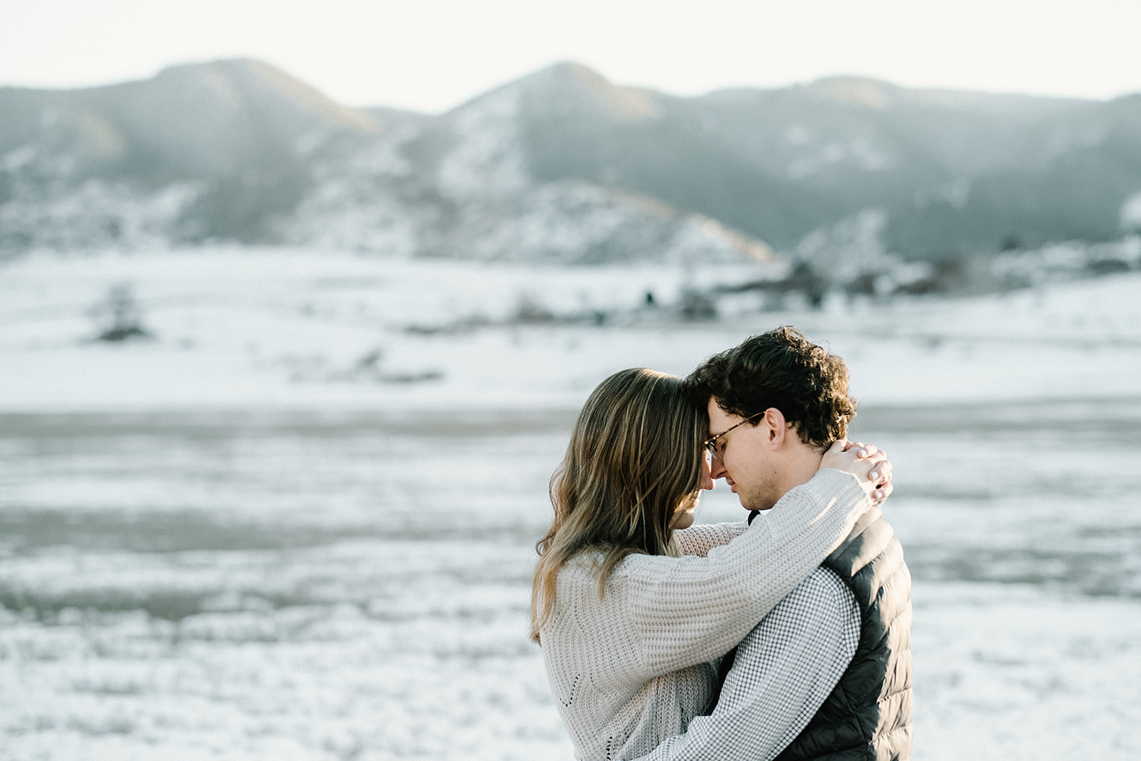engaged couple embrace beneath the snowy Rocky Mountains